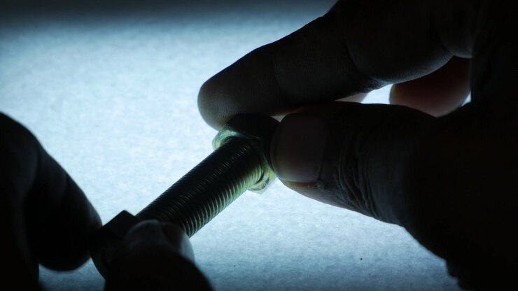 Hands Fastening Metal Hex Nut onto Threaded Bolt from Side Angle