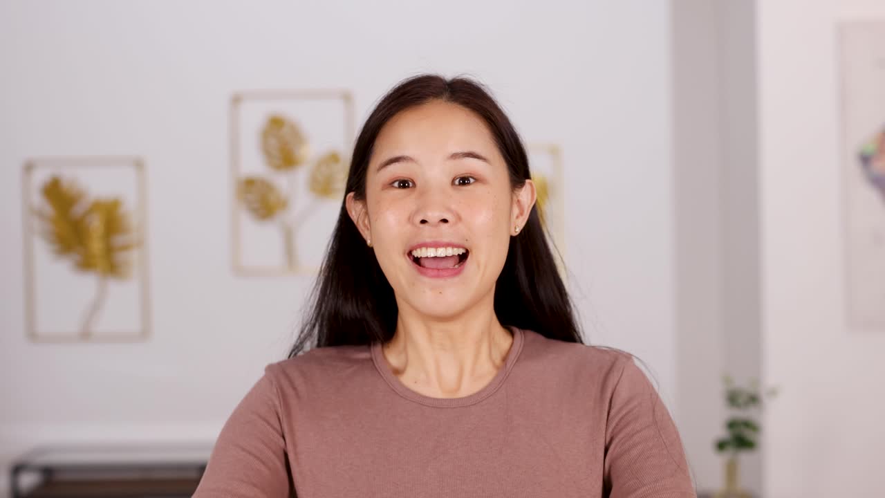 Smiling woman in casual clothes celebrates success with raised fists in bright, modern home interior