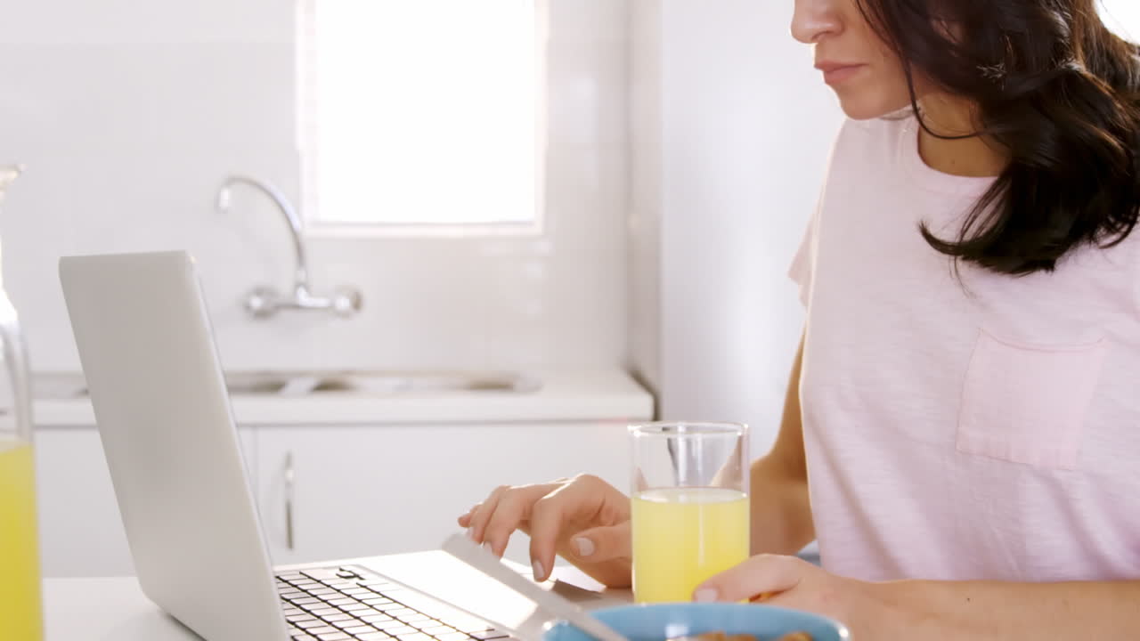 mujer tomando su desayuno y usando su portátil