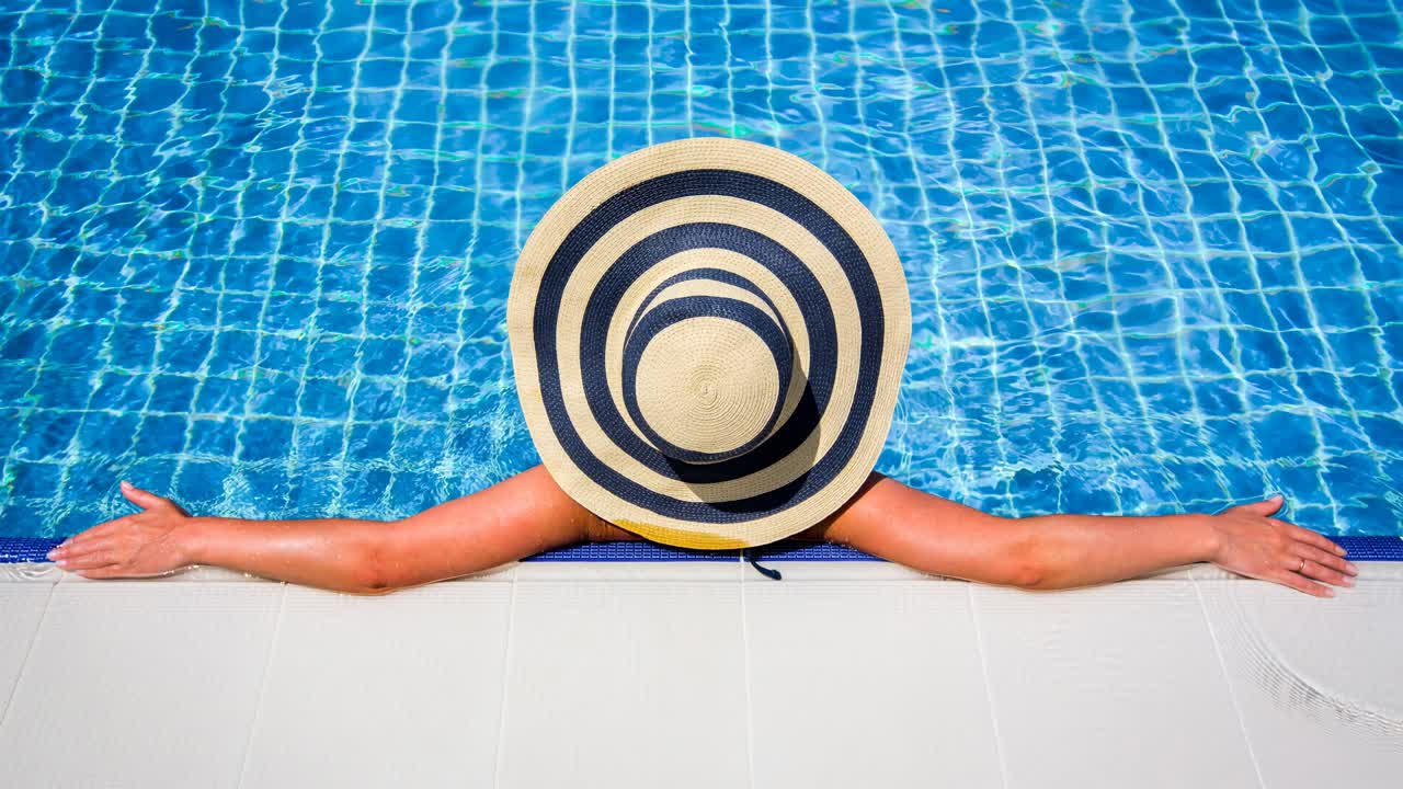 Woman in straw hat relaxing swimming pool