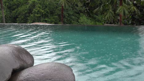 tropical summer rain splashing into swimming pool. close up of swimming pool during storm and rain drops falling into water.