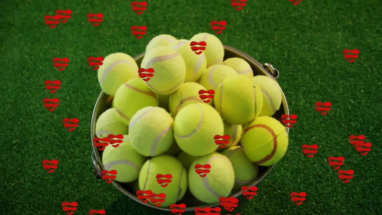 One second in, bucket holding yellow tennis balls on green turf getting swirling red hearts overlay