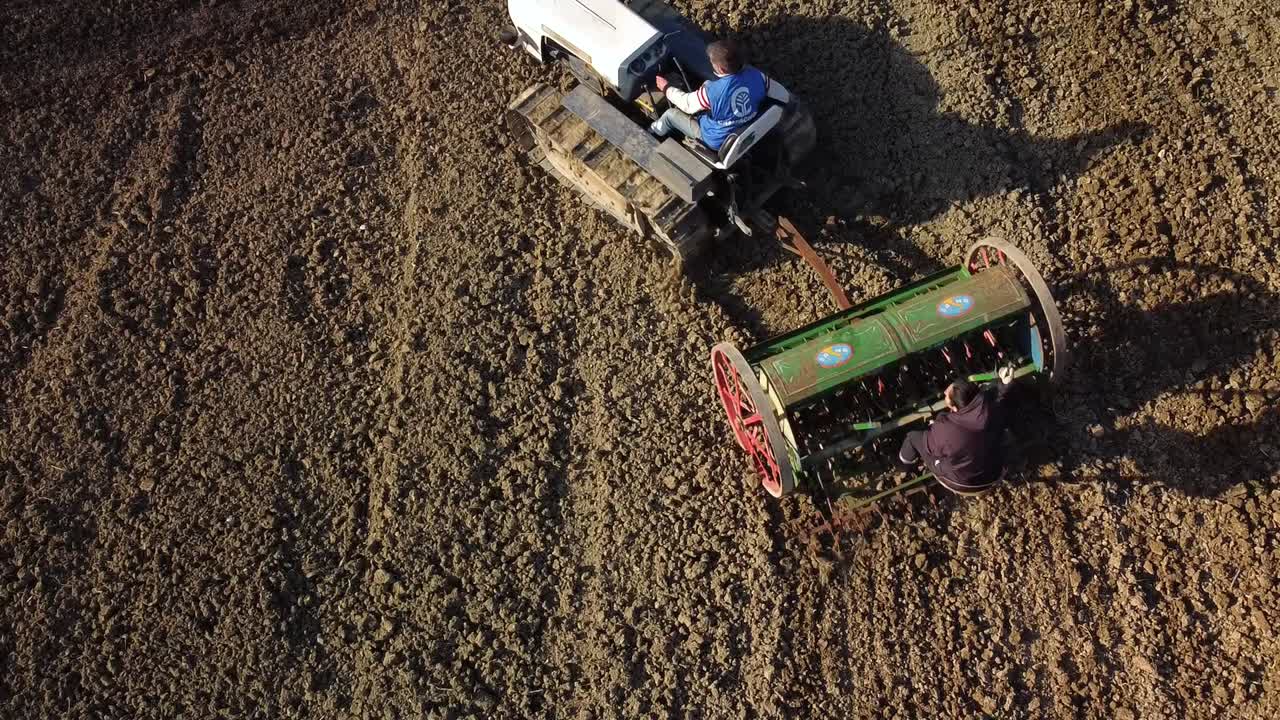 aerial shot of sowing the field with white crawler tractor and green seeder, bird's eye shot