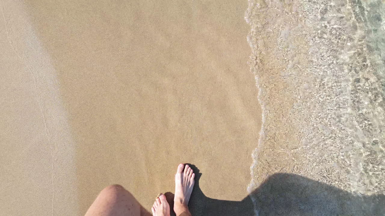 A person walking barefoot on a sandy beach with waves gently washing over the feet