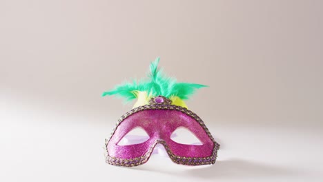 Video-of-pink-masquerade-mask-with-green-and-yellow-feathers-on-white-background-with-copy-space