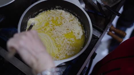 hand stirs hot bagna cauda in a saucepan as golden melted butter swirls into garlic and anchovies, forming a creamy emulsion during the traditional cooking process of this piedmontese italian sauce.