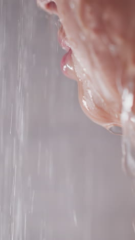 water pours on woman face in bathroom closeup. sensual lady with plump lips takes warm shower in washroom. beauty and glamour lifestyle concept