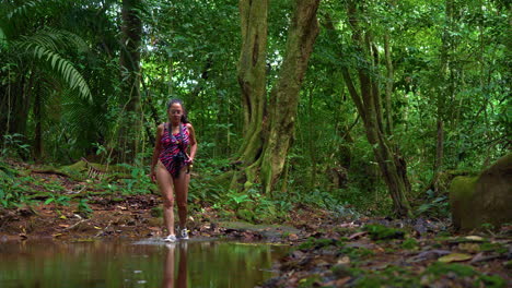 slow motion shot of a young woman crossing a jungle creek in swimwear in caimito