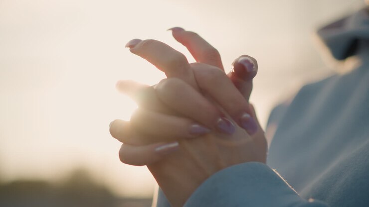 Close-up van dame met verzorgde nagels die een polsbeweging maakt in een blauwe trui, warm zonlicht dat rond de handen gloeit en de sierlijke polsbeweging benadrukt tijdens een fitnessroutine in de buitenlucht