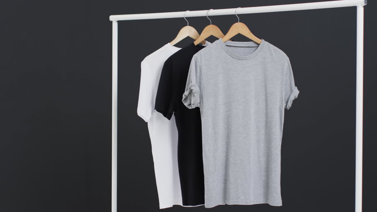 Video of three white, black and grey t shirts on hangers and copy space on black background