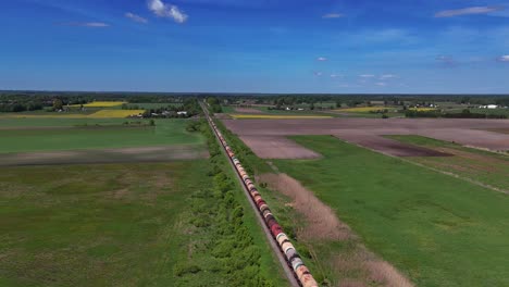 a long cargo train travels through lush green countryside under a clear blue sky