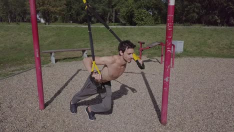 Young-fitness-male-athlete-working-out-with-TRX-in-the-park,-outdoors-in-covid-time