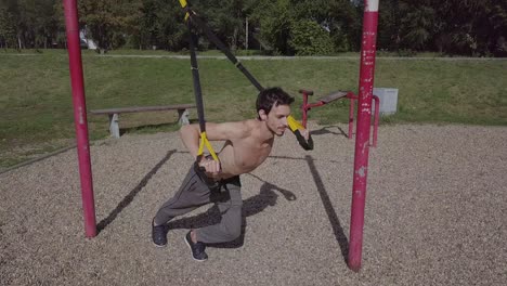 joven atleta masculino de fitness trabajando con trx en el parque, al aire libre en tiempo de covid