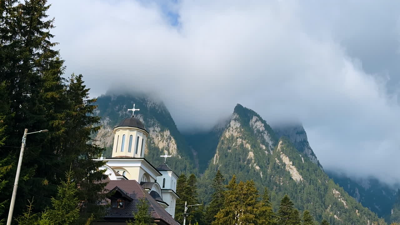 Thick clouds or fog covering the tops of the high mountains. Orthodox church is located near the mount. The Bucegi Mountains of the Southern Carpathians, Romania