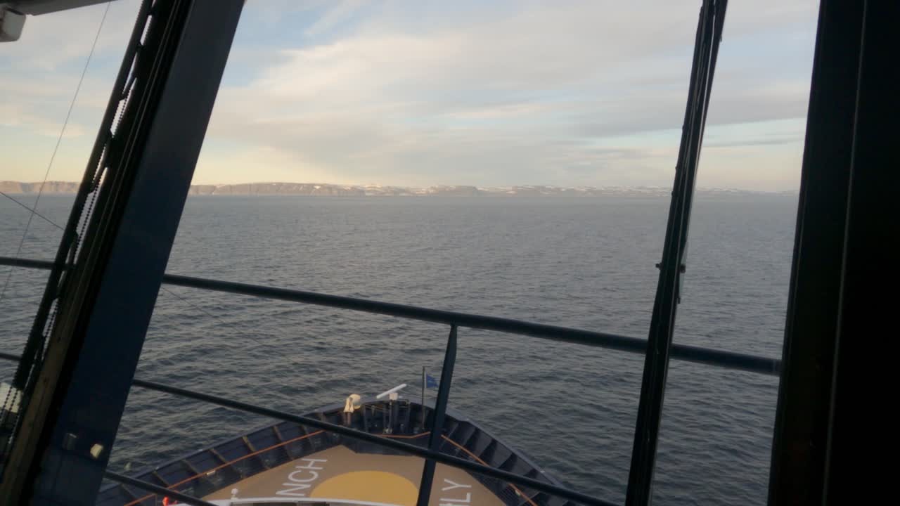POV vom Deck eines Kreuzfahrtschiffes, das durch arktische norwegische Gewässer nahe dem Nordkap fährt. Dramatische Küstenklippen, ruhige See und die Atmosphäre der Mitternachtssonne schaffen ein atemberaubendes nordisches Reiseerlebnis.