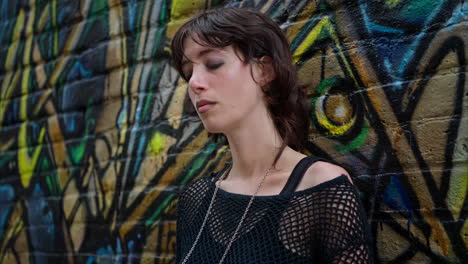 retrato de moda al aire libre de una mujer joven de estilo alternativo apoyándose en una pared cubierta de graffiti en la calle de la ciudad de londres, reino unido, en tiempo real.