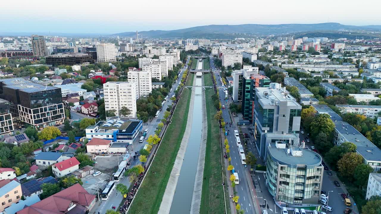 Aerial drone video showing a long line of people walking along Bahlui River in Iasi, Romania, heading toward the Metropolitan Cathedral for Saint Parascheva pilgrimage