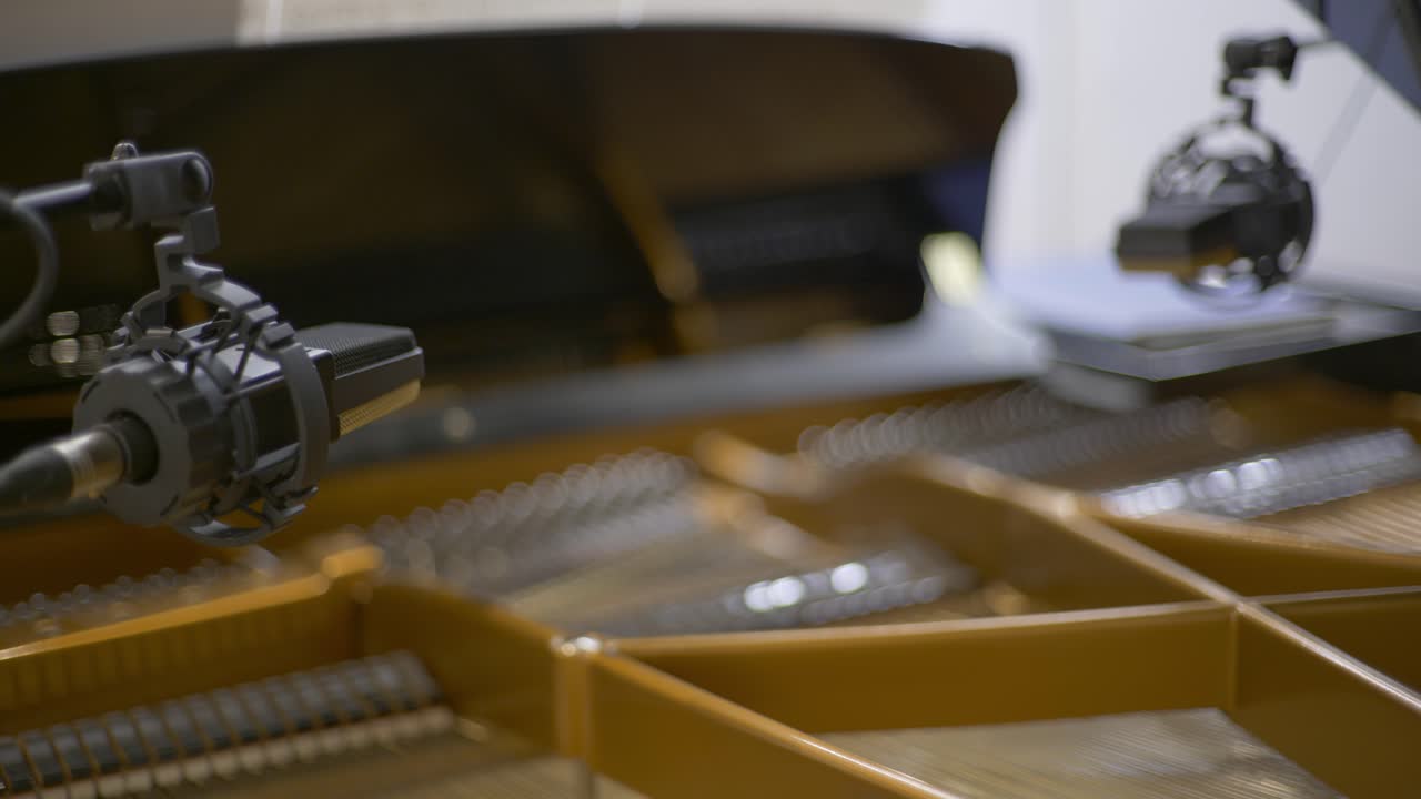 Racking Focus of two condenser microphones positioned over the strings of an open concert grand piano in a recording studio during a recording session