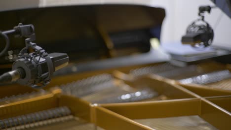 racking focus of two condenser microphones positioned over the strings of an open concert grand piano in a recording studio during a recording session