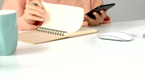 cerrar a las jóvenes mujeres asiáticas dueñas de negocios usando la aplicación de teléfono inteligente y tomar notas en la oficina.