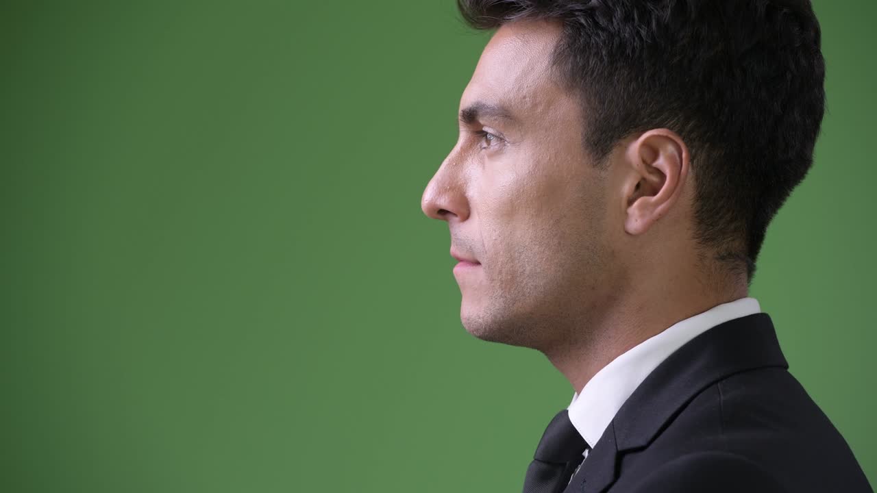 Young handsome Hispanic businessman against green background