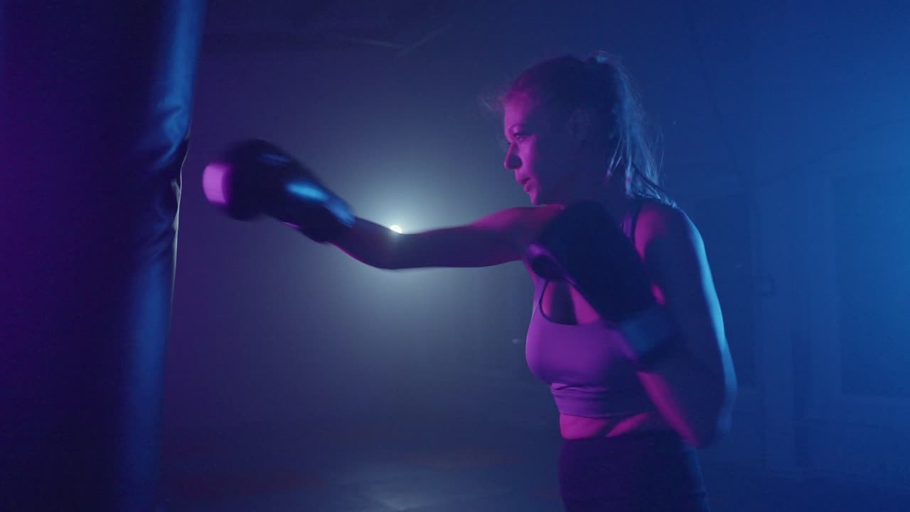 Mujer decidida entrenando boxeo con un saco de boxeo en un gimnasio iluminado con neón