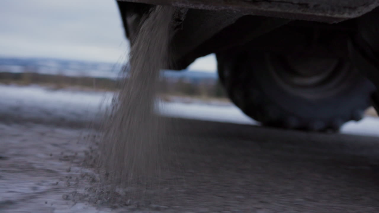노르웨이 북부 스칸디나비아의 서리가 내린 겨울 눈 덮인 아침에 자갈이 있는 활주로의 그립력을 개선하는 트레일러 소금 도로가 있는 대형 녹색 클라스 트랙터 트럭