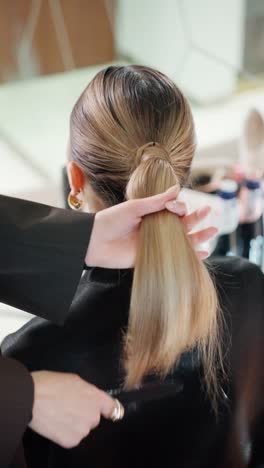 a stylist brushes woman's hair blonde ponytail, tightly secured and ready for a transformation in a professional salon setting