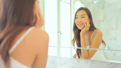 Mujer-Asiática-Revisando-Y-Tocando-La-Piel-De-Su-Cara-Cerca-Del-Espejo-Sonriendo-En-El-Baño-Por-La-Mañana-En-Cámara-Lenta