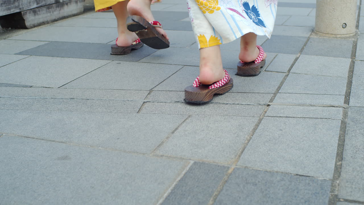 ángulo lateral de hermosas chicas caminando en kimono tradicional usando sandalias de madera en un puente en kyoto, japón iluminación suave