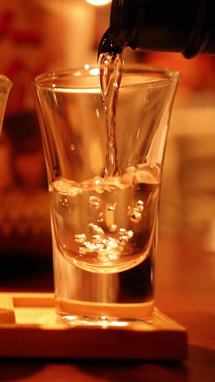 A vertical shot showing clear sake liquid filling a glass on a wooden stand.