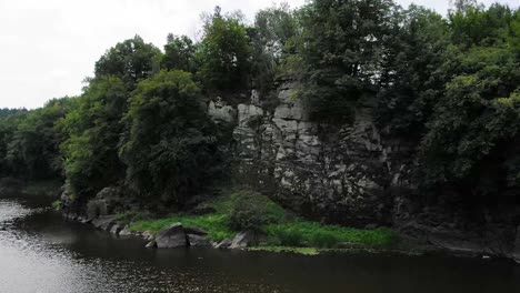 Aerial-View-of-Steep-Cliff-on-Rivers-Edge-With-Thick-Surrounded-by-Thick-Forestry