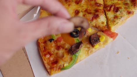 fingers grab a slice of roasted mushrooms from a vegetarian pizza with olives