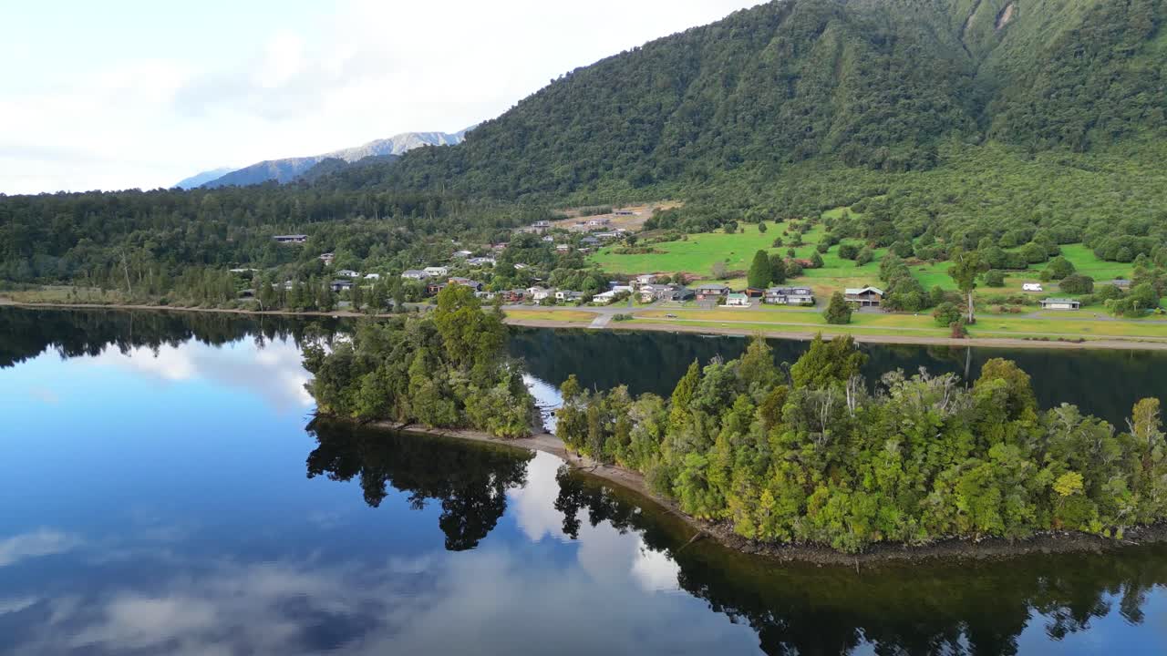 Slow-Motion Drone Flyover of Mirror Lake with Village and Bush-Covered Foothills – New Zealand