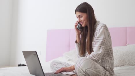 Hübsches-Mädchen-Im-Pyjama-Im-Bett,-Das-Telefoniert-Und-An-Einem-Laptop-Arbeitet