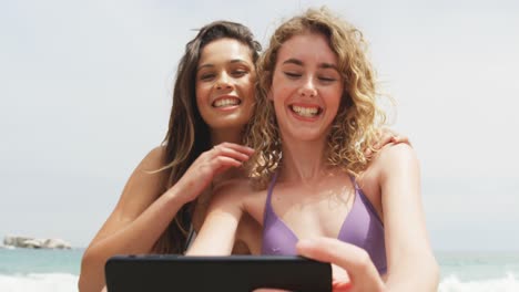 vista frontal de dos amigas de raza mixta tomando una selfie con un teléfono móvil en la playa 4k