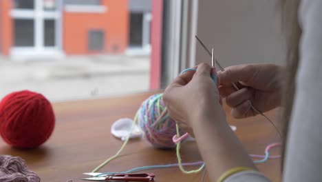 woman crotchets with multicolored yarn using needle and hook, balls of yarn in back