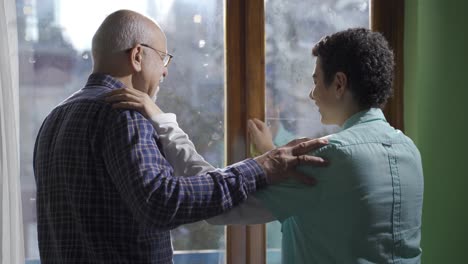 Old-grandfather-and-grandson-are-chatting-happily,-looking-out-the-window.