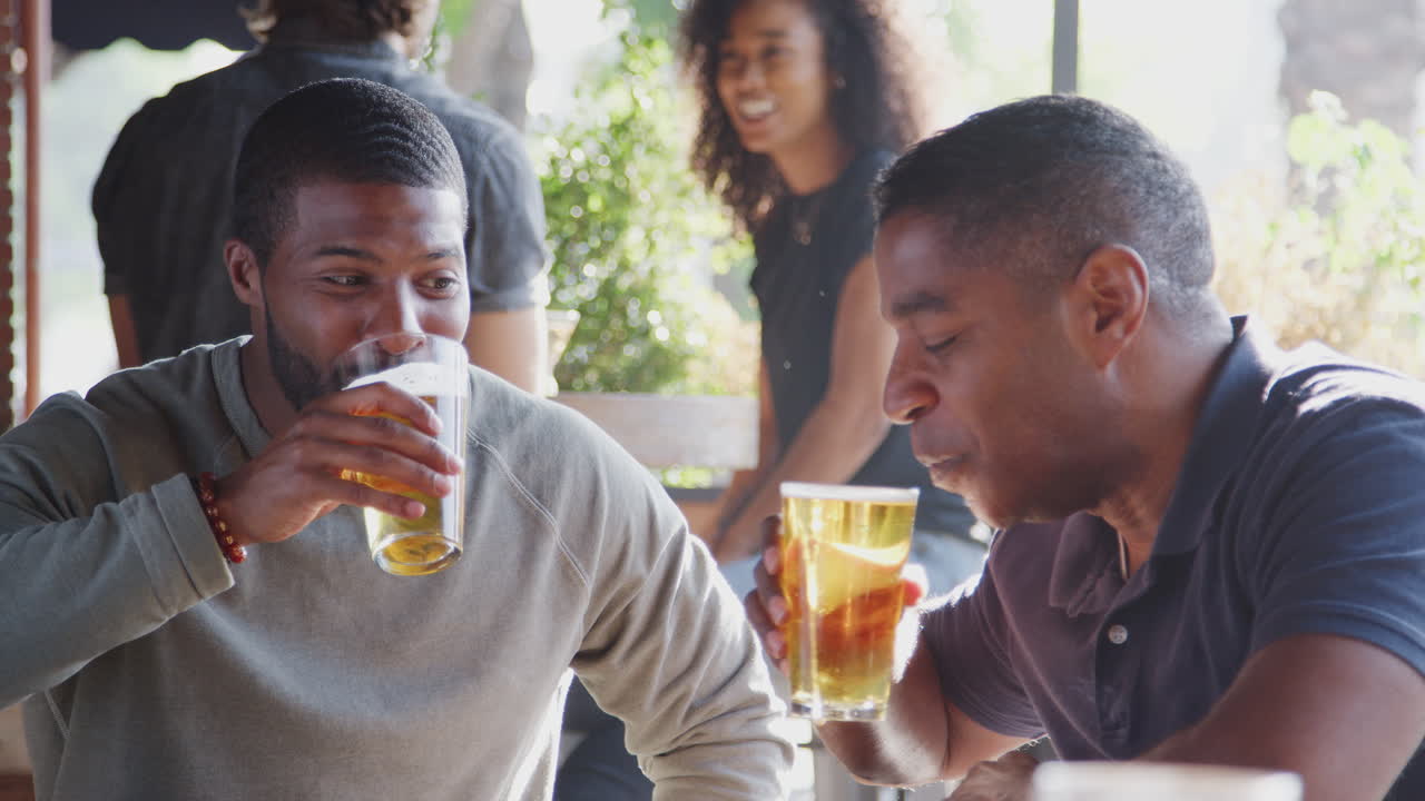 Two Male Friends Meeting In Sports Bar Making Toast Together