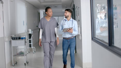 Diverse-male-and-female-doctors-discussing-work-using-tablet-in-hospital-corridor,-slow-motion