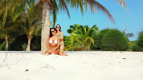 Women-massaging-with-sunscreen-on-paradise-exotic-beach-sitting-on-white-sand-under-shadow-of-palm-tree-on-tropical-island-in-Seychelles