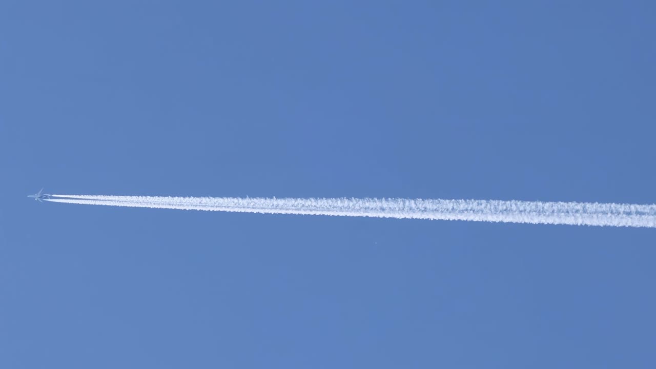 A jet plane leaves a distinct contrail across a clear blue sky, showcasing high-altitude flight dynamics.