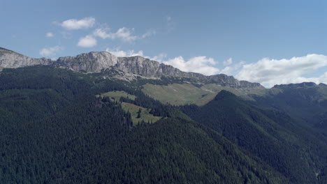 Luftaufnahme-Eines-Hohen-Felsigen-Berges,-Umgeben-Von-Tiefen-Tälern-Mit-Grünen-Tannenwäldern-An-Einem-Tag-Mit-Blauem-Himmel-Und-Wenigen-Wolken