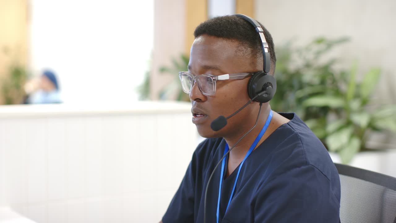 Afroamerikansk mann mottar anrop, har på seg hodesett, vipper hodet og håndterer kundesamtale ved skrivebordet.