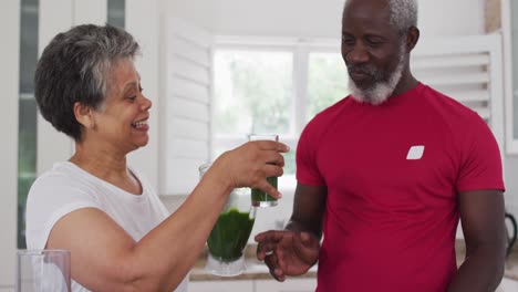 hombre y mujer afroamericanos mayores bebiendo frutas y verduras en casa.