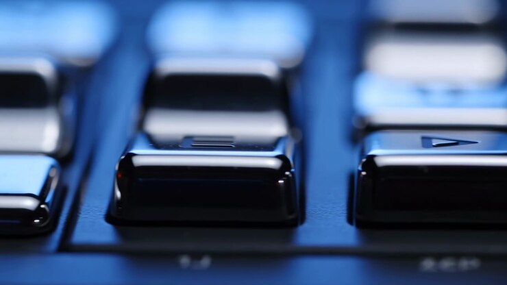 Close-up scene of glossy black keypad showing front-row rectangular keys with play symbol and menu bars, cool studio lighting, shallow depth, and shifting focus across polished surface