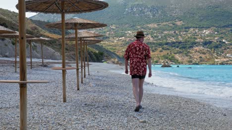 Un-Turista-Adulto-Caminando-Relajado-A-Lo-Largo-De-La-Costa-De-Guijarros-En-Un-Hermoso-Día-Soleado-En-La-Playa-De-Agia-Kiriaki,-Zola-En-Kefalonia,-Grecia