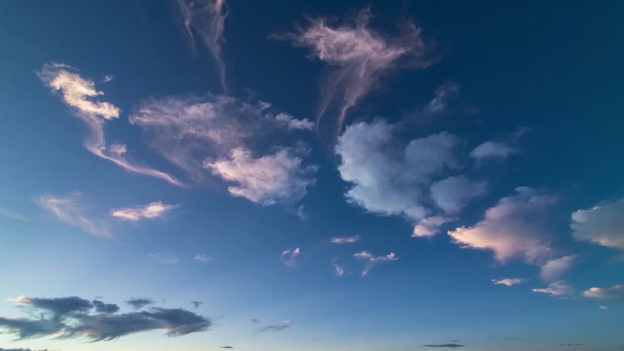 Skiftende cumulus-klynge driver og strækker sig på åben himmel over lav horisont, vind trækker slør