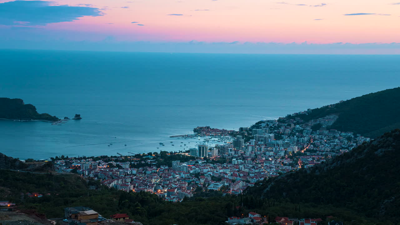 해변 도시 부바(budva), 몬테네그로(montenegro)의 낮에서 밤까지의 시간 경과는 빛나는 주황색 하늘에서 시작하여 도시의 빛으로 빛나는 어두운 하늘로 전환됩니다.