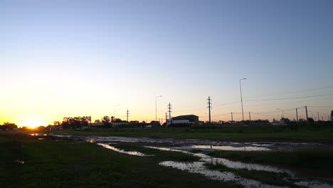 Trucks-pass-right-to-left-on-a-rural-route-at-dusk,-with-a-flooded-service-road-in-the-foreground